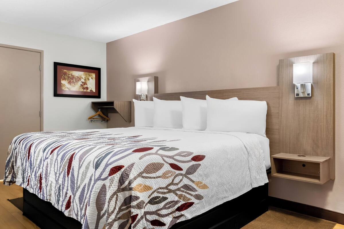 Une chambre d’hôtel avec un lit, une table de chevet, une lampe fixée au mur et un tableau encadré.