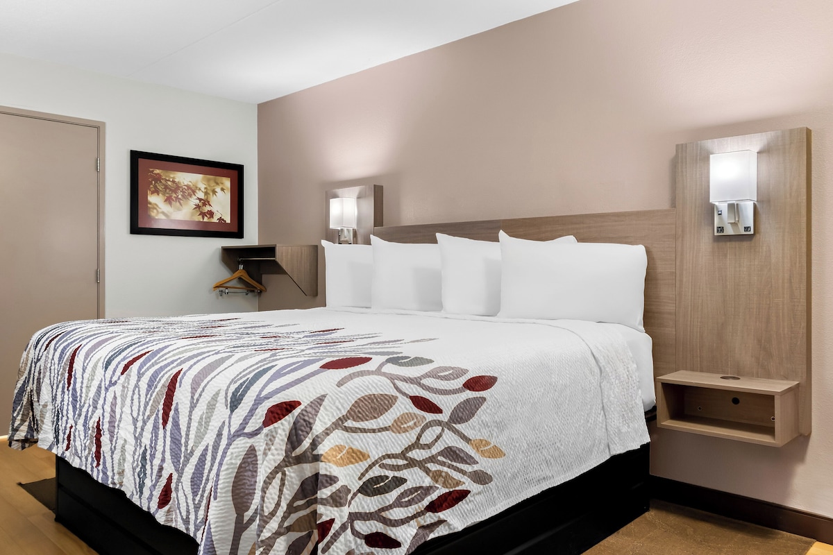 Ein Hotelzimmer mit einem Bett, einem Nachttisch, einer Wandlampe und einem gerahmten Bild.