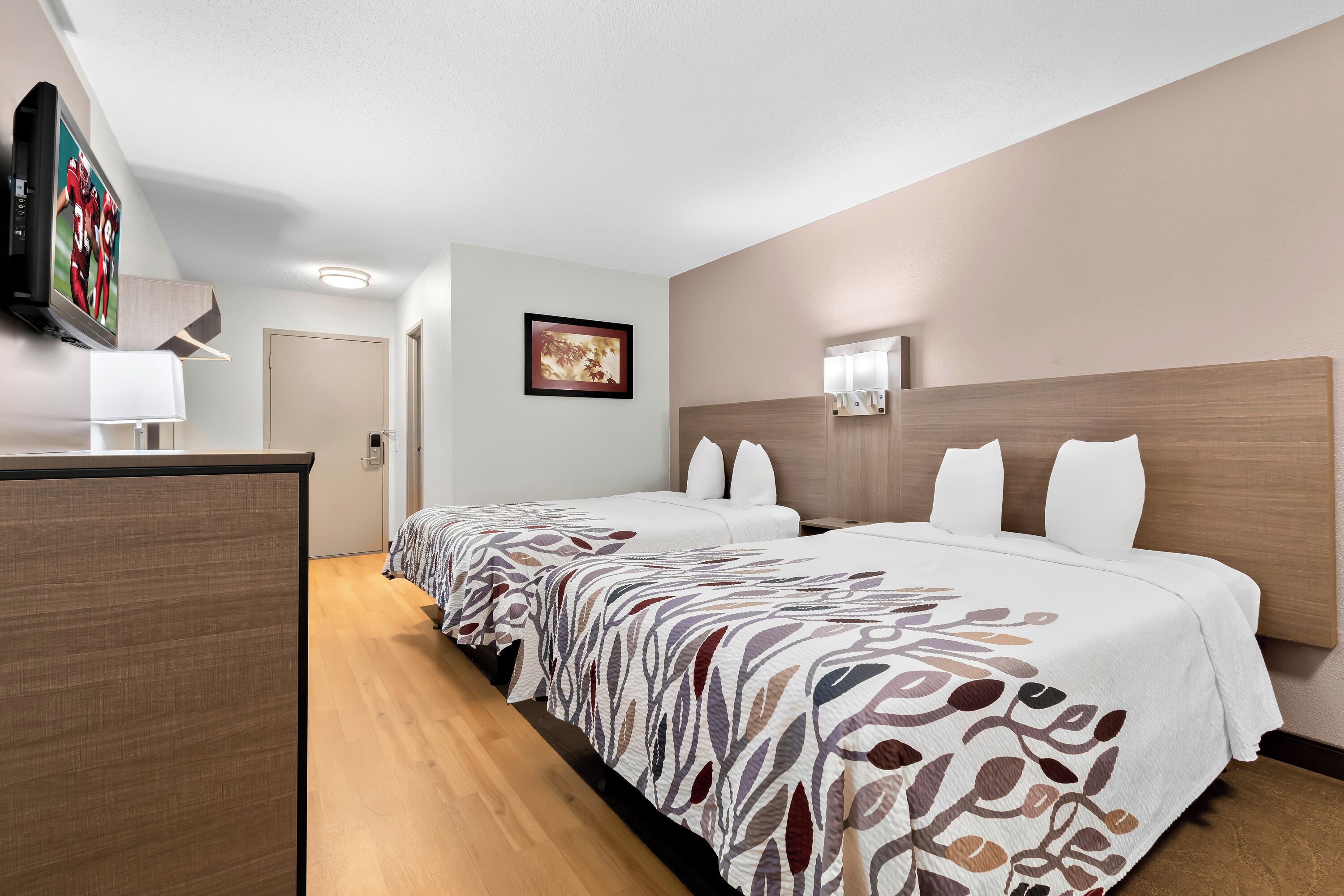 A hotel room with two beds, a TV, a desk, and a framed picture on the wall.