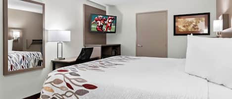 Una habitación de hotel con una cama grande, un escritorio, un televisor montado en la pared y una puerta.