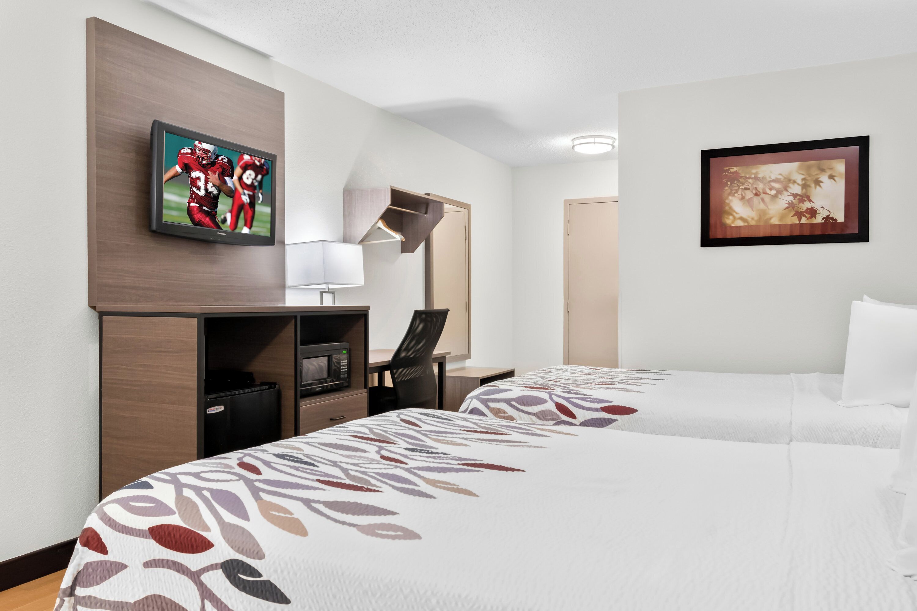 Quarto de hotel com duas camas, uma televisão, uma mesa com abajur e obras de arte nas paredes.
