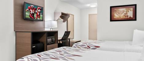 Quarto de hotel com duas camas, uma televisão, uma mesa com abajur e obras de arte nas paredes.