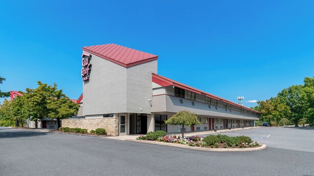 A motel with a red roof and a stone facade, featuring a parking lot and a small garden area. - Red Roof Inn Harrisburg North (Harrisburg)