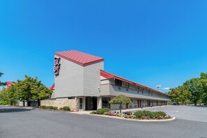 A motel with a red roof and a stone facade, featuring a parking lot and a small garden area. - Red Roof Inn Harrisburg North (Harrisburg)