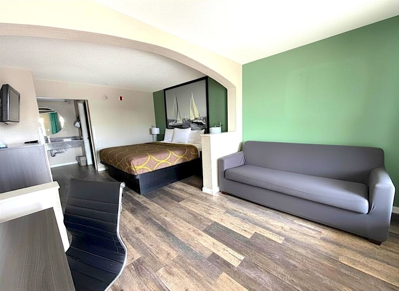 Une chambre d’hôtel avec un lit, un canapé gris, un bureau avec une chaise et un miroir.