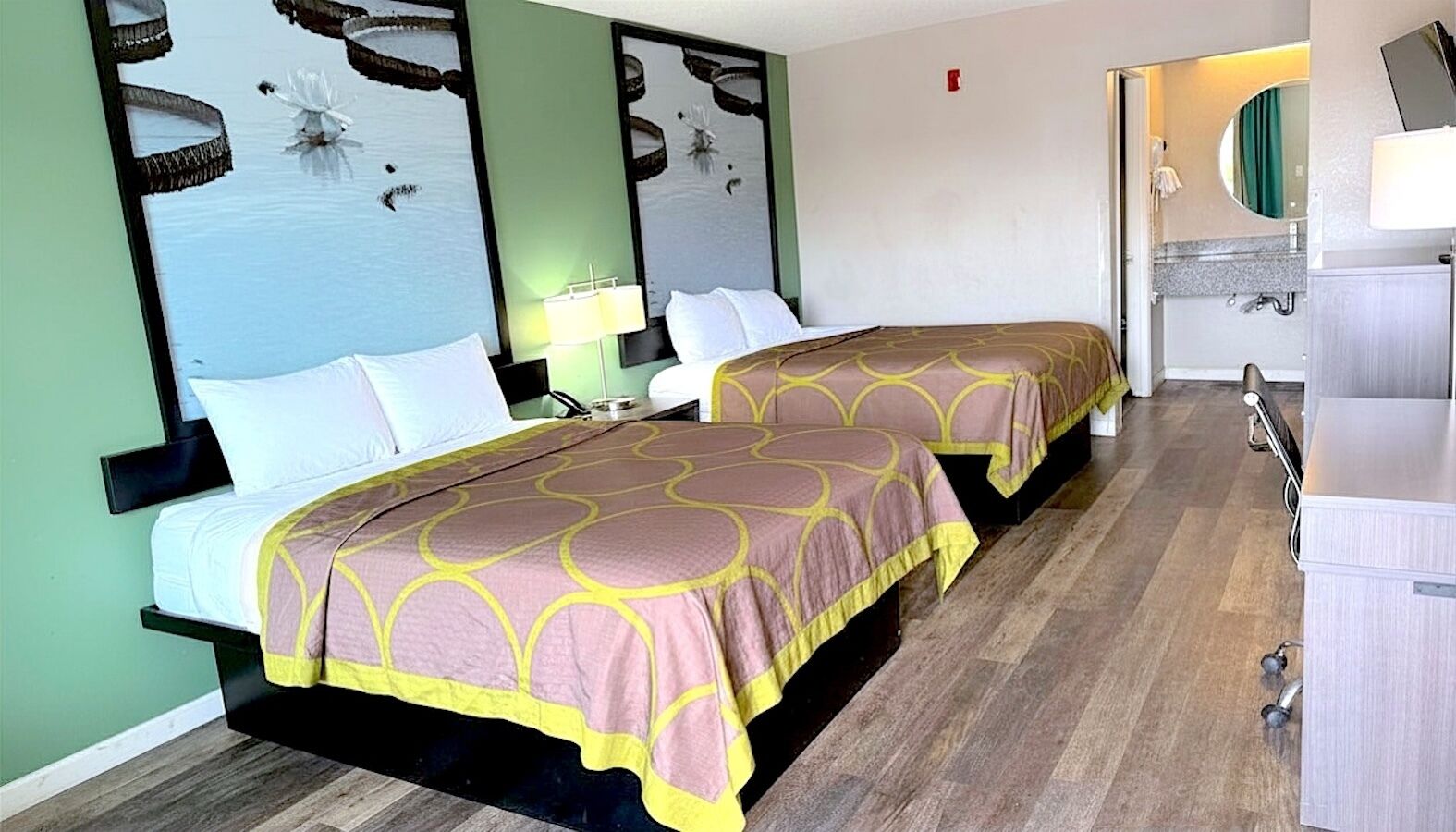 A hotel room with two beds, a mirror, a sink, and a wooden floor.