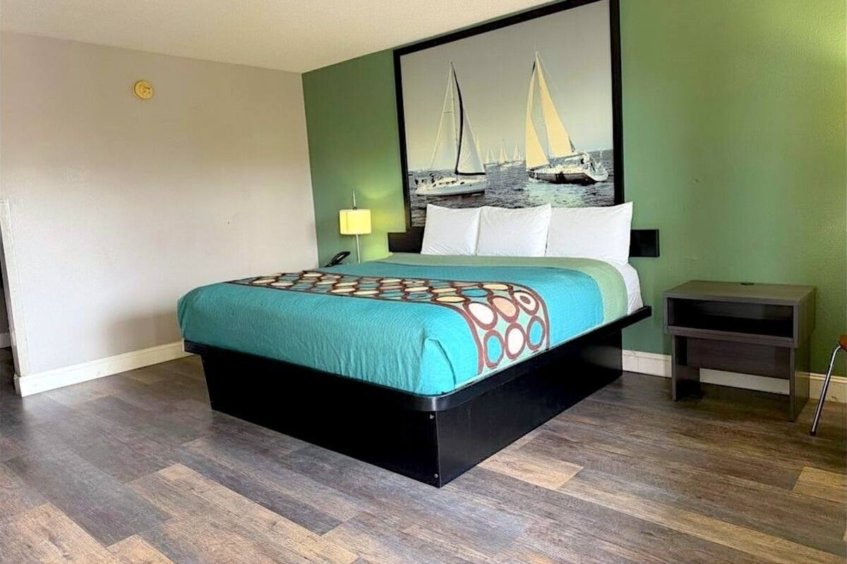 Ein Hotelzimmer mit einem Bett, einem Nachttisch, einer Lampe und einer Wanduhr.