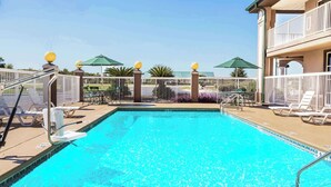 Una piscina con indicador de profundidad de 3 pies, rodeada por una cerca blanca, con sillas de descanso y sombrillas.