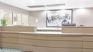 Un área de recepción con mostrador, un cartel de bienvenida en un marco grande y una planta en maceta.
