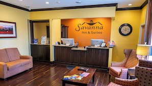 A reception area with a reception desk, computers, a coffee table with an American flag, and patterned chairs. - Savanna Inn & Suites (Savanna)