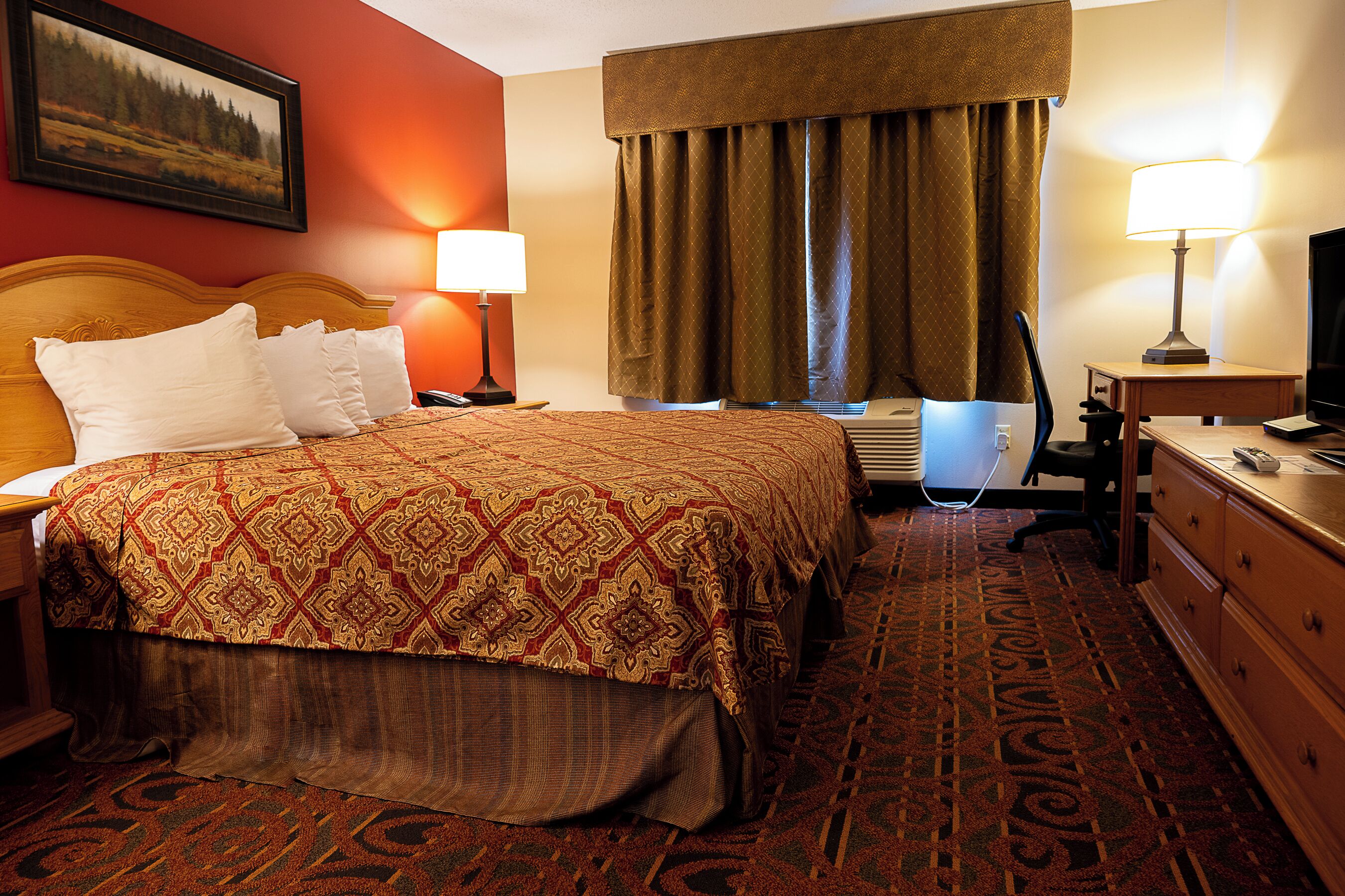 A hotel room with a large bed, a desk, a chair, a television, and a lamp.