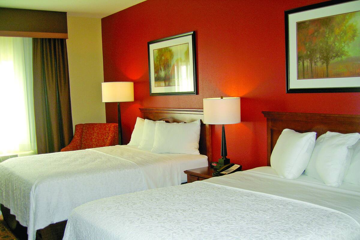 Habitación de hotel con dos camas, una pared roja y un cuadro enmarcado sobre las camas.