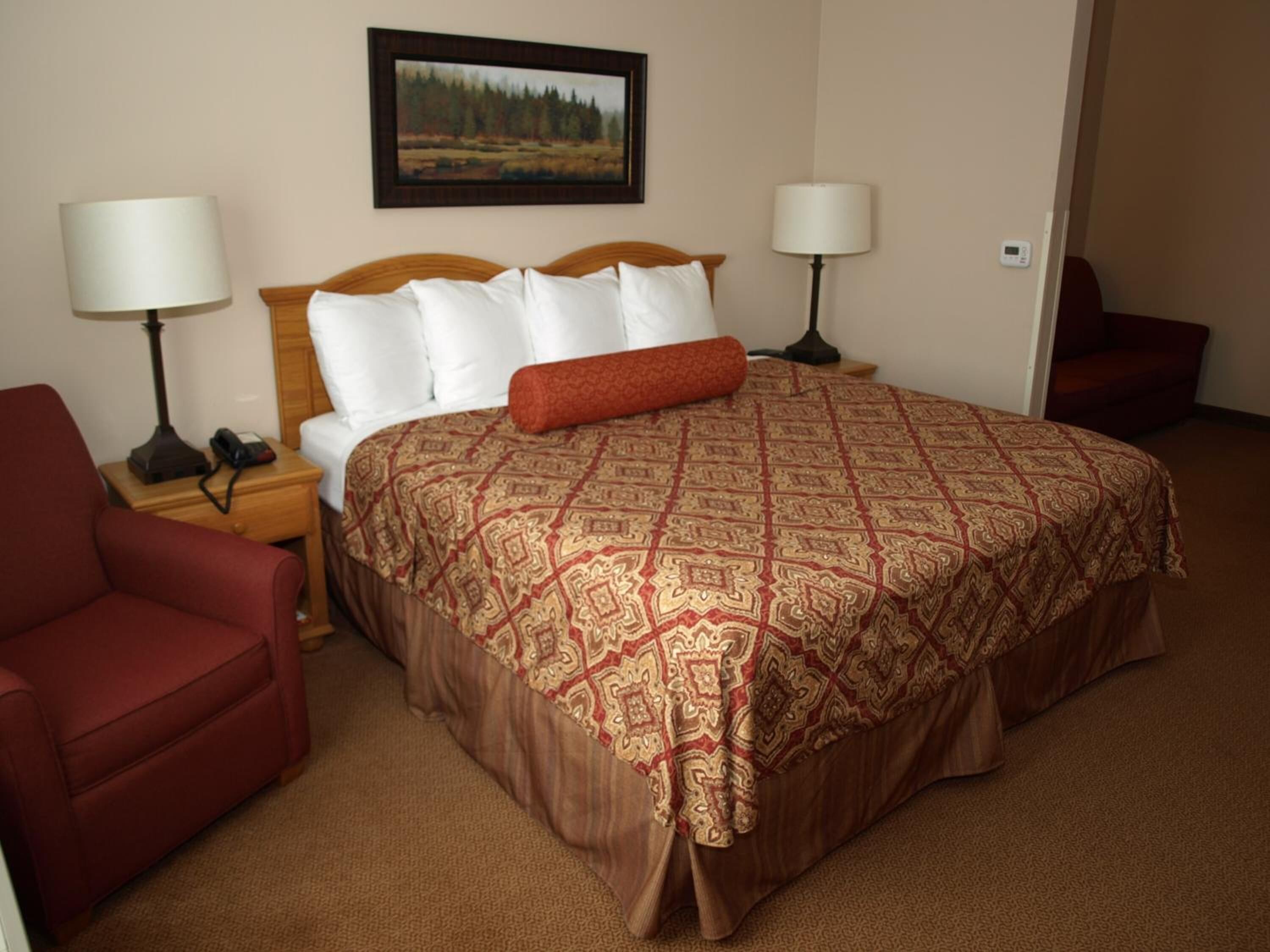A hotel room with a large bed, two bedside tables, a red armchair, and a painting on the wall.