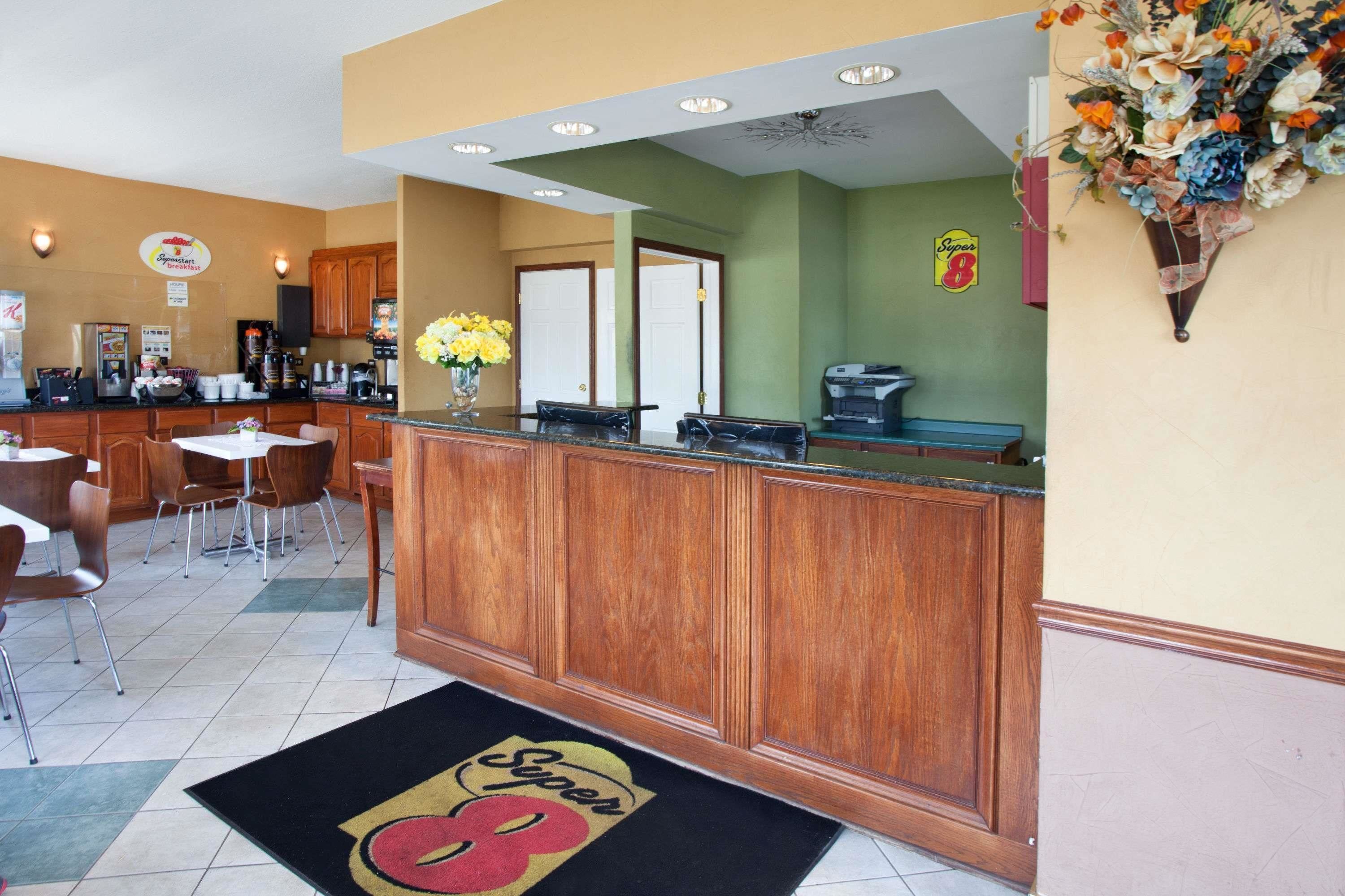 A hotel lobby with a reception desk, wooden cabinets, a coffee machine, and a flower arrangement.