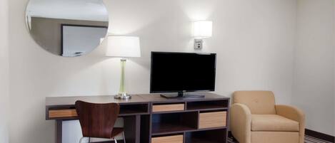 Habitación de hotel con escritorio, silla, televisor, lámpara y sofá.
