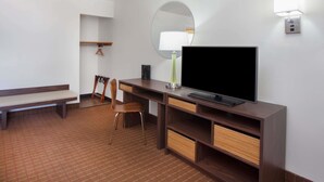 A hotel room with a wooden desk, a flat-screen TV, a chair, a bench, a round mirror, and a wall-mounted lamp. - Super 8 by Wyndham Chicago/Rosemont/O'Hare/SE (River Grove)