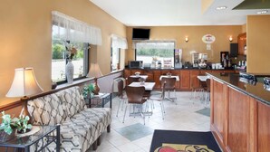 A hotel room with a sofa, dining table, chairs, a kitchen area, and a TV. - Super 8 by Wyndham Chicago/Rosemont/O'Hare/SE (River Grove)