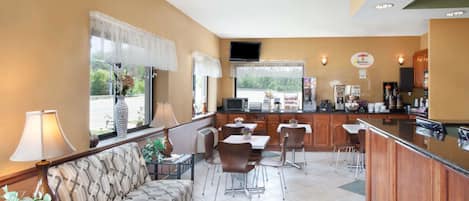 A hotel room with a sofa, dining table, chairs, a kitchen area, and a TV.