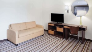 A hotel room with a sofa, a TV, a desk with a lamp, and a mirror. - Super 8 by Wyndham Chicago/Rosemont/O'Hare/SE (River Grove)