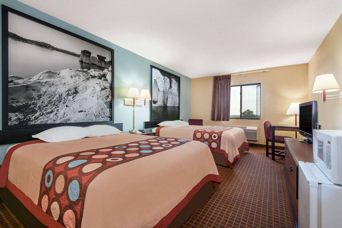 Habitación de hotel con dos camas, un escritorio, un televisor y un cuadro grande en la pared.