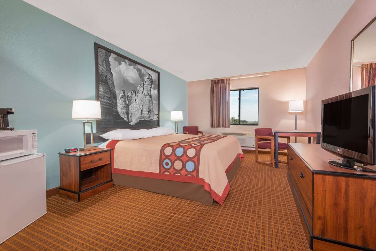 Habitación de hotel con cama, lámparas de noche, escritorio con televisor, microondas y ventana grande.
