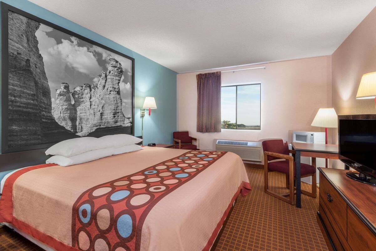 Habitación de hotel con una cama grande, un escritorio con televisor, microondas y ventana con cortinas.