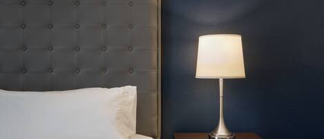 Una cama bien hecha con cabecera capitonada, una mesita de noche con una lámpara y una pared azul oscuro.