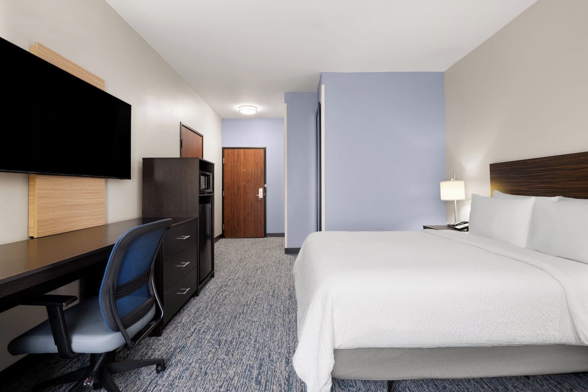 Una habitación de hotel con cama, escritorio, silla, televisión y una puerta.