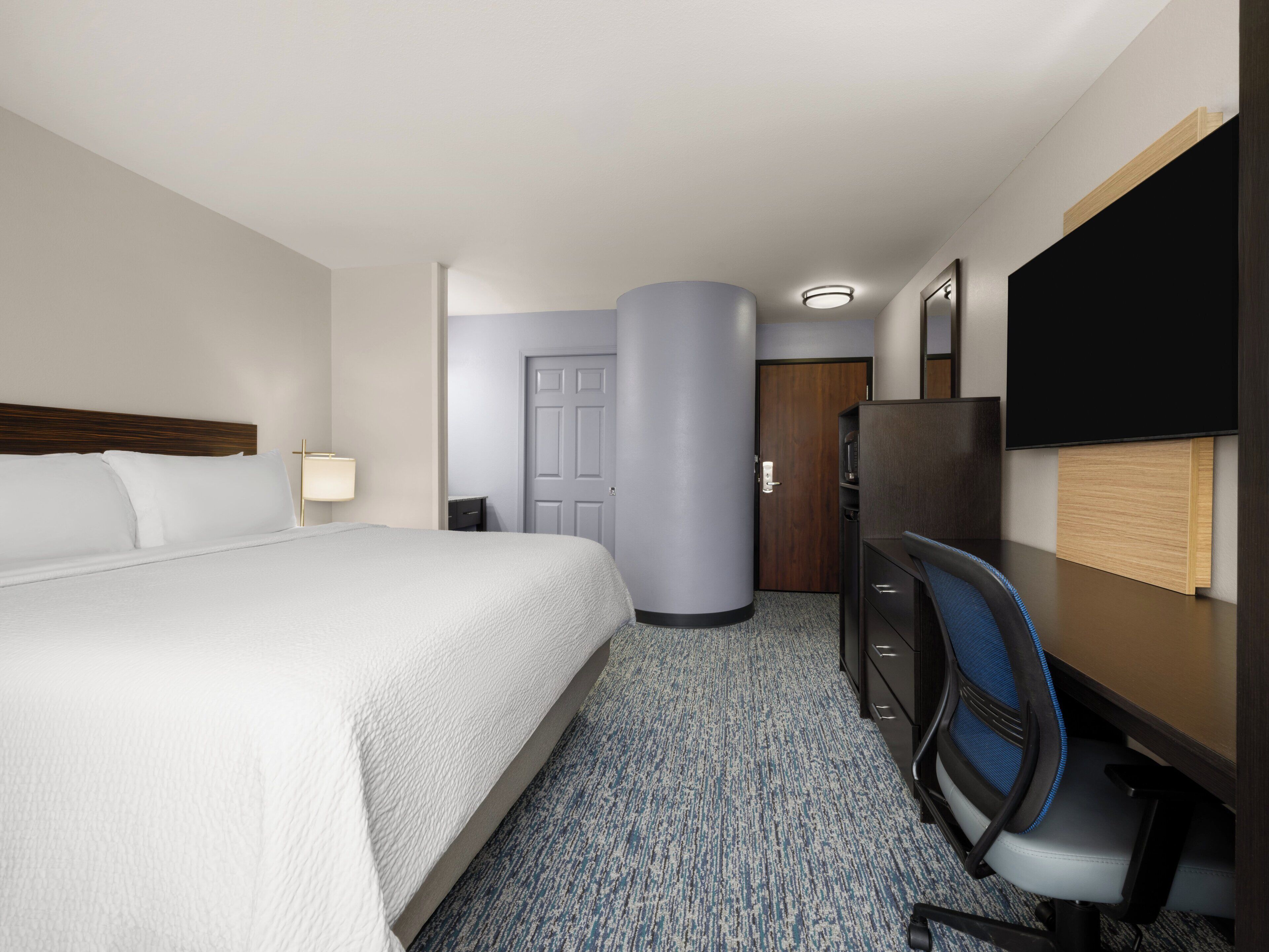 A hotel room with a bed, desk, chair, TV, and a door.