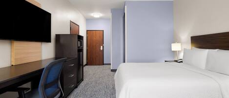 A hotel room with a bed, desk, chair, television, and a door.