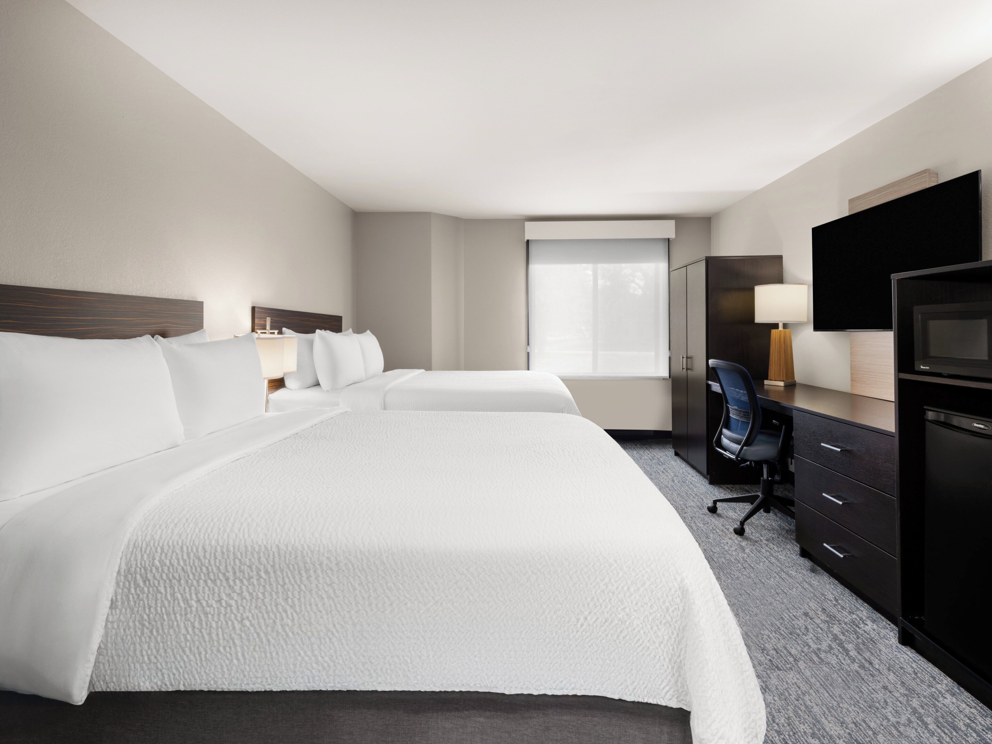 A hotel room with two beds, a desk, a chair, a TV, and a wardrobe.