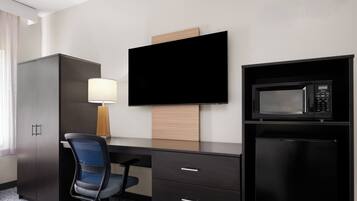 Habitación de hotel con escritorio, silla, televisor, microondas y armario.