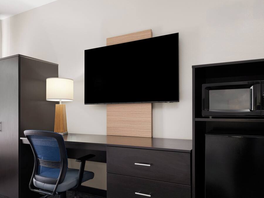 A hotel room with a desk, a chair, a television, a microwave, and a cabinet.