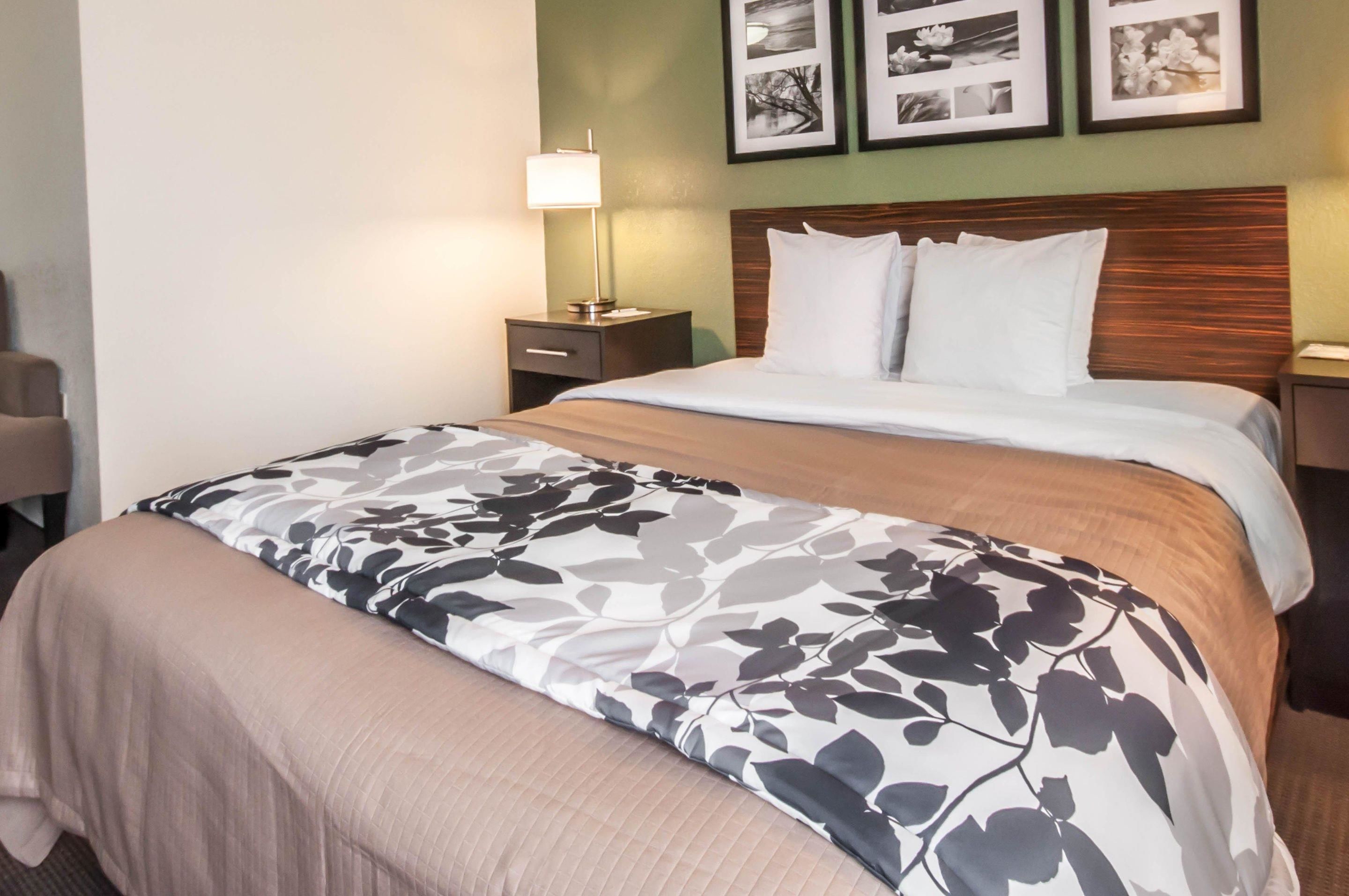 A hotel room with a bed, a nightstand with a lamp, and framed pictures on the wall.