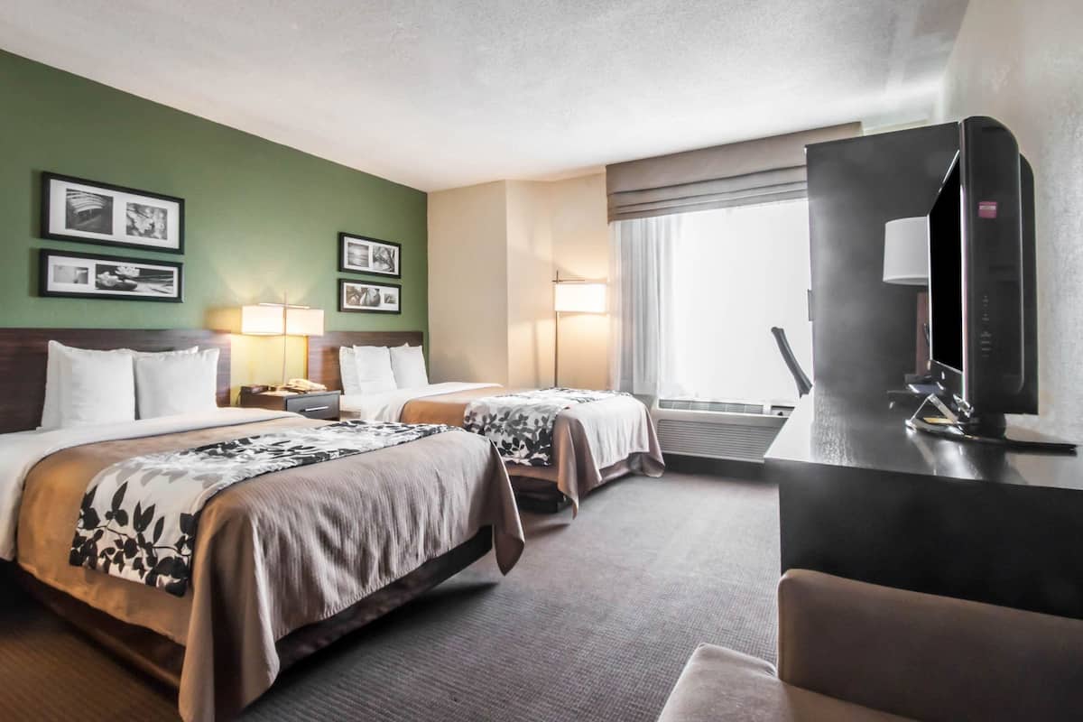 A hotel room with two beds, a desk, a TV, and a large window with curtains.