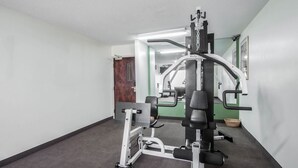 Une salle de sport équipée de matériel d’exercice, avec un miroir et une porte donnant sur une autre pièce.