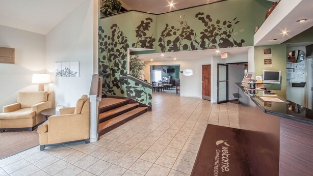 Un hall d’hôtel comprenant un comptoir d’accueil, un espace salon, un escalier et un mur orné d’un motif végétal.