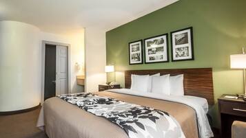 Una habitación de hotel con una cama grande, una mesita de noche con una lámpara y una pared decorada con cuadros.