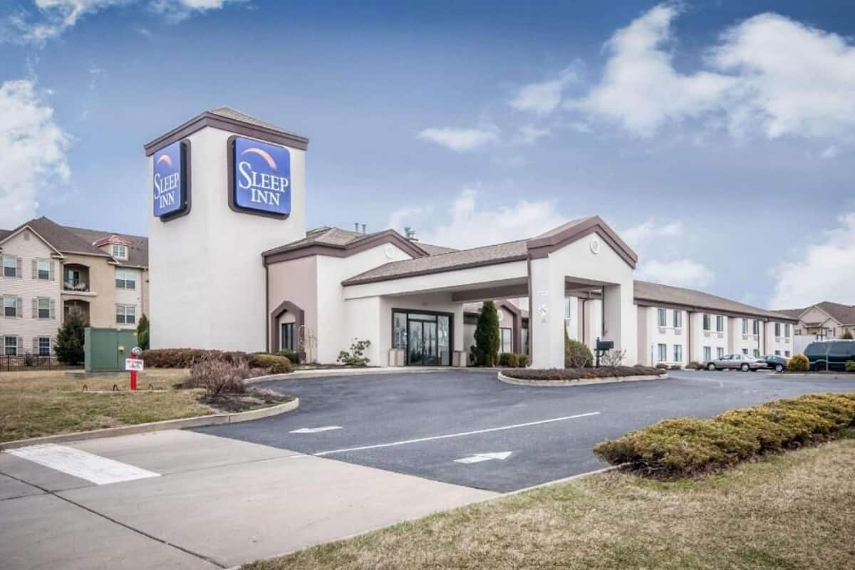 A Sleep Inn hotel with a central entrance, a parking lot, and a clear sky.