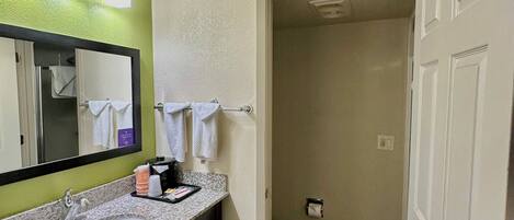 Baño con encimera de granito, lavamanos, espejo y retrete visible a través de una puerta abierta.
