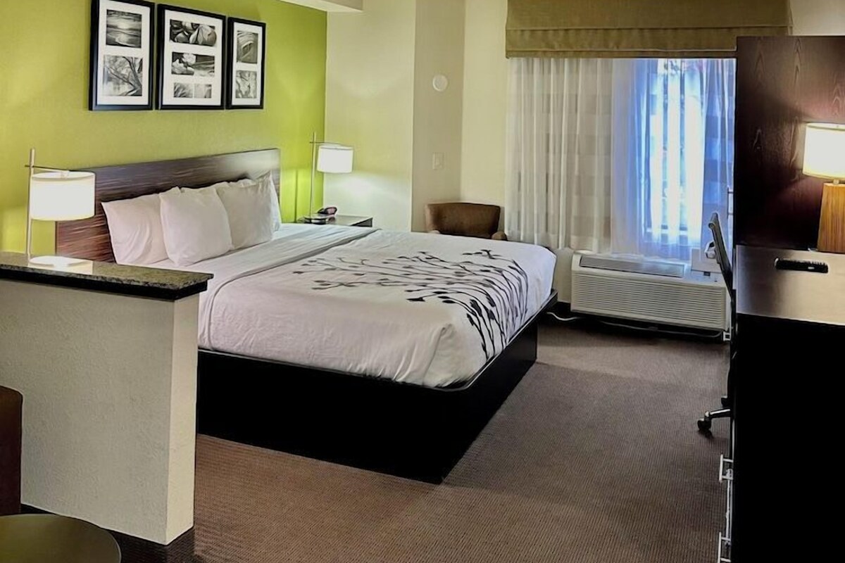 A hotel room with a bed, bedside tables, a desk, a chair, and a window with curtains.