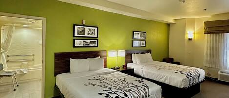 A hotel room with two beds, a bathroom with a shower, and a small seating area.