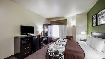A hotel room with a bed, a desk with a computer, a television, a chair, and a window with curtains.