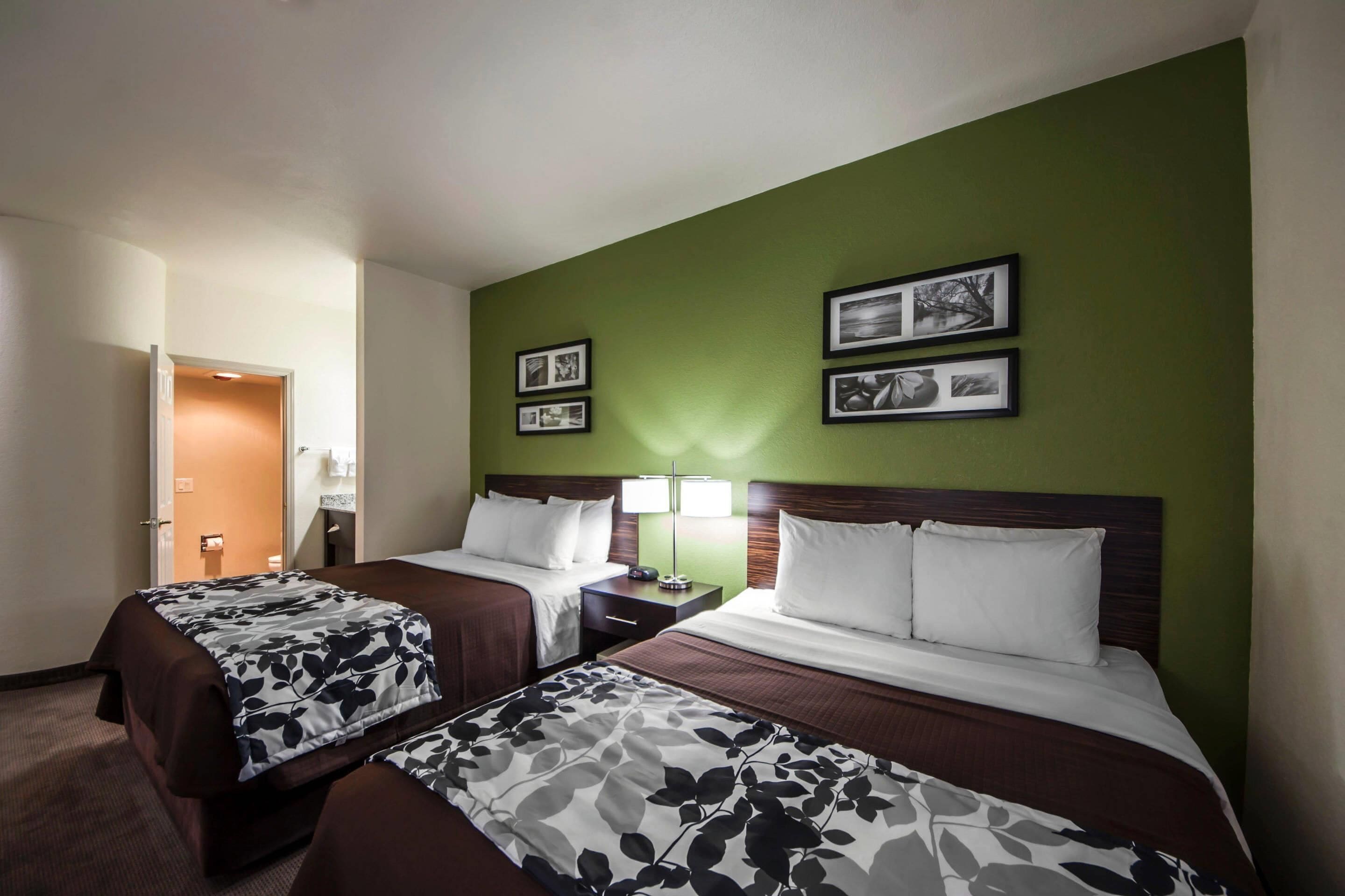 Ein Hotelzimmer mit zwei Betten, einer grünen Akzentwand, gerahmten Bildern und einem Nachttisch mit Lampe.
