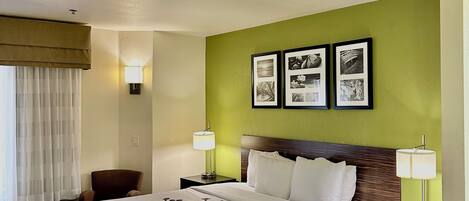 A hotel room with a large bed, two bedside lamps, a chair, a desk, and a wall with framed pictures.