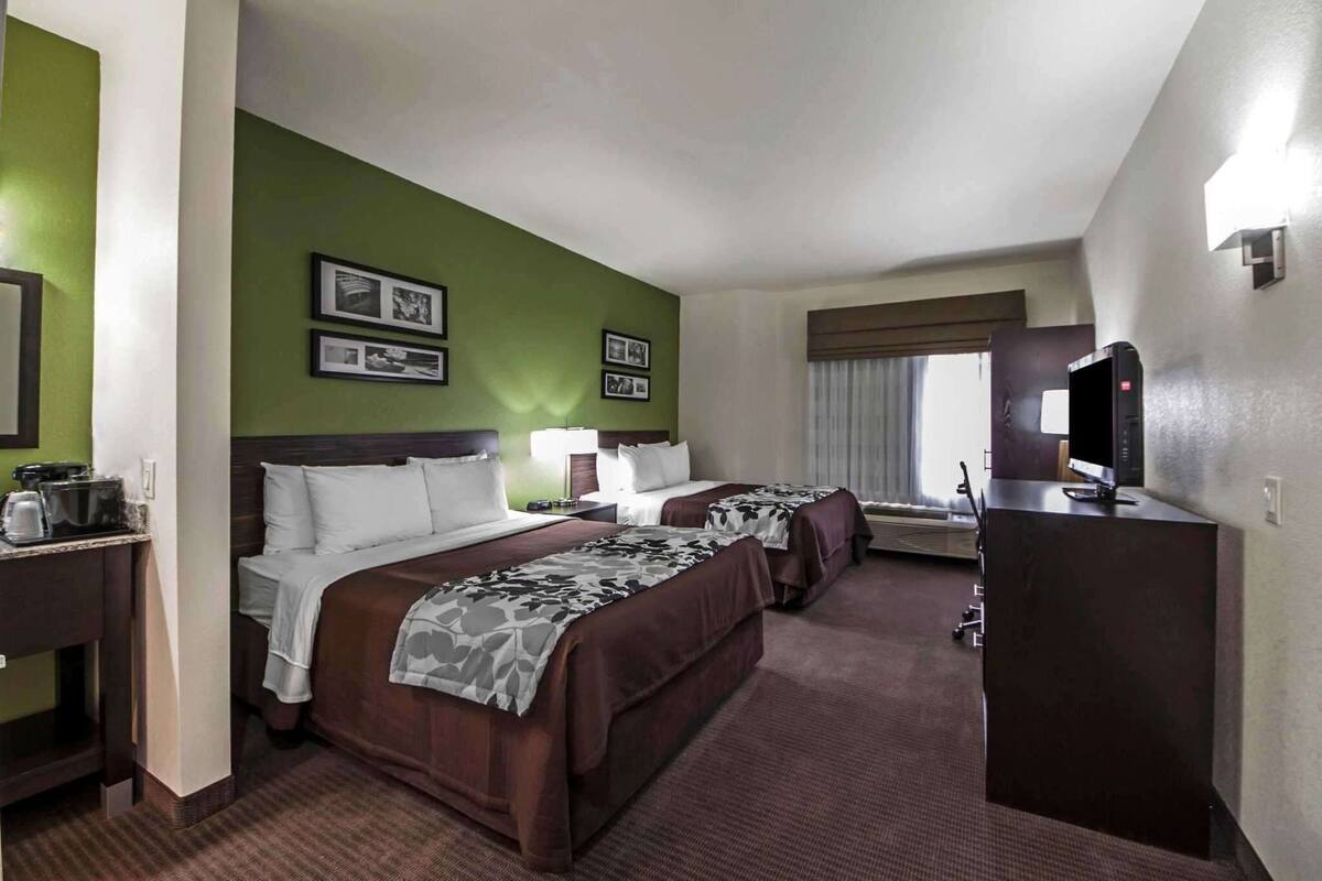 A hotel room with two beds, a desk, a TV, and a window with curtains.
