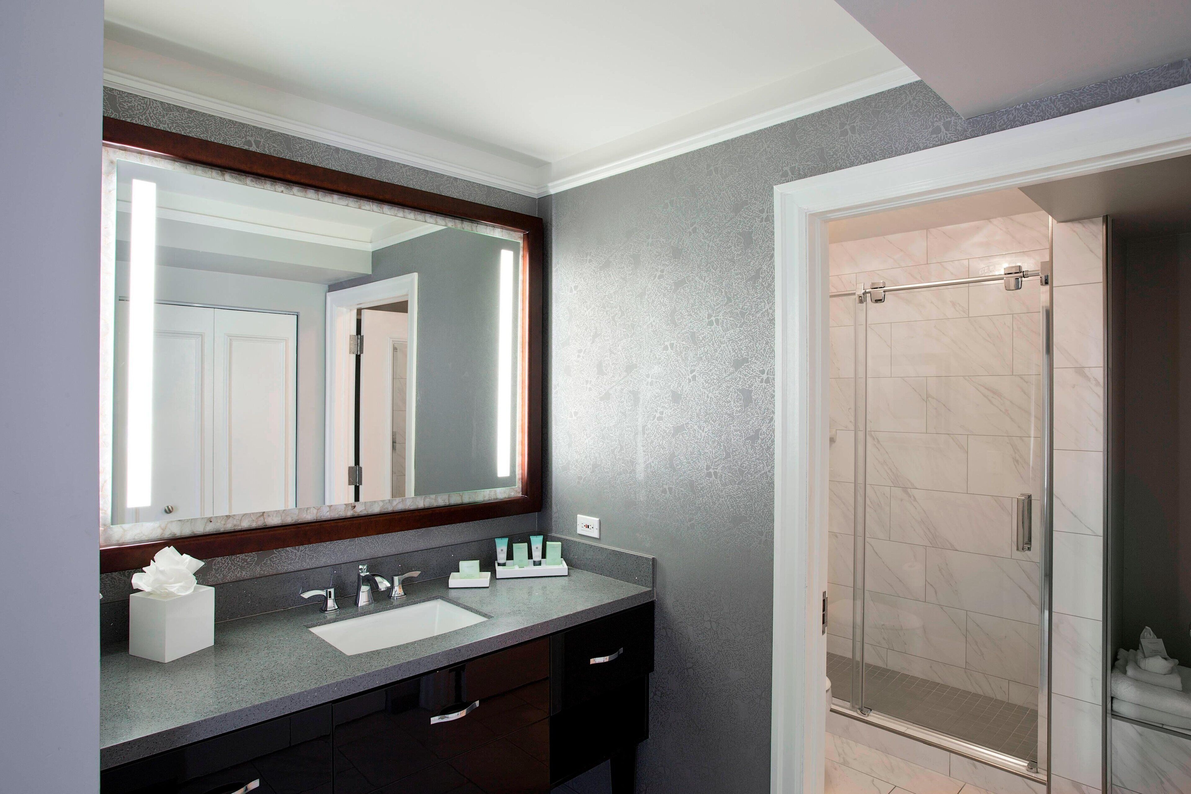 A bathroom with a large mirror, a sink, and a shower.