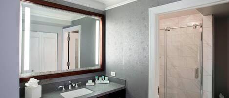 A bathroom with a large mirror, a sink, and a shower.