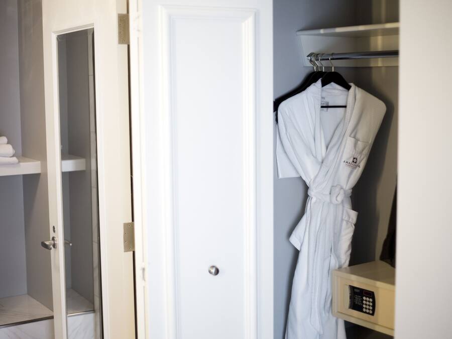 Habitación de hotel con una puerta blanca, una bata colgada en un perchero y un estante con toallas dobladas.