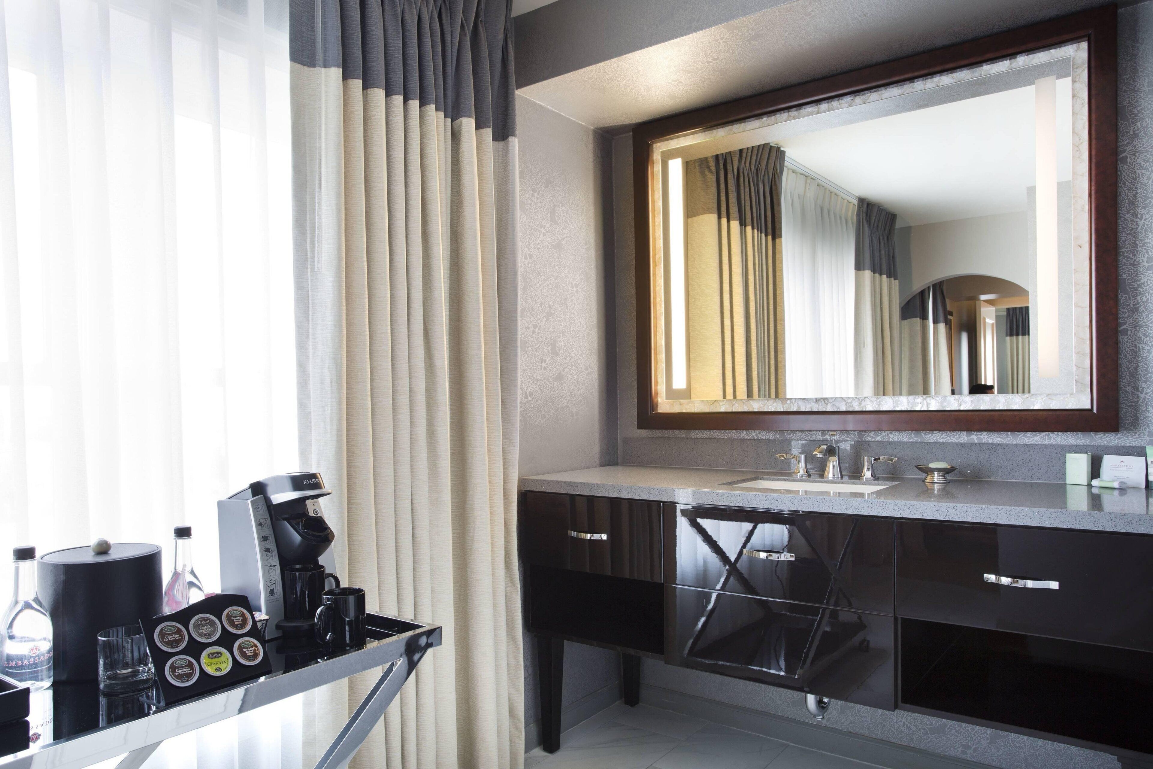 Un bagno moderno con uno specchio grande, mobili scuri e una macchina da caffè su un vassoio.
